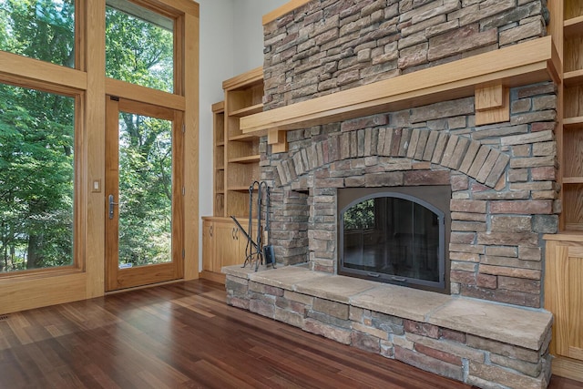 unfurnished living room with a stone fireplace, built in features, a high ceiling, and dark hardwood / wood-style floors