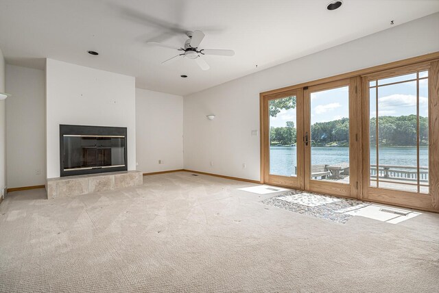 unfurnished living room featuring ceiling fan, a fireplace, a water view, and a healthy amount of sunlight