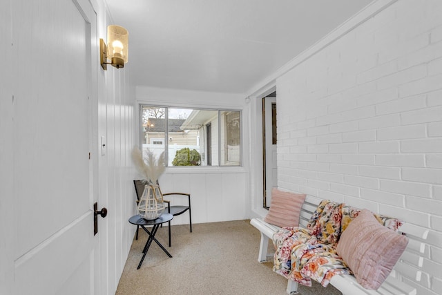 sitting room featuring crown molding, light colored carpet, and brick wall