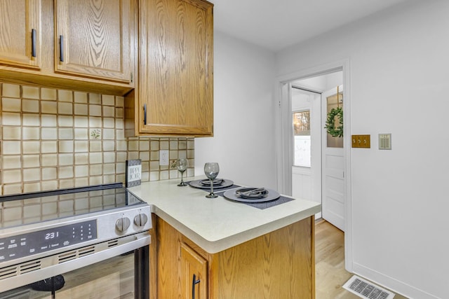 kitchen with tasteful backsplash, light hardwood / wood-style flooring, and stainless steel range oven