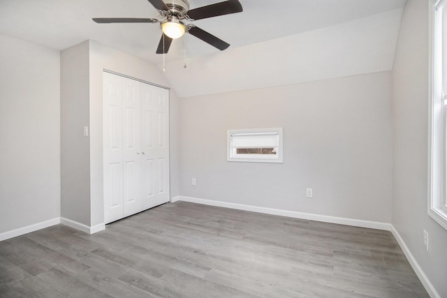 unfurnished bedroom with ceiling fan, a closet, light hardwood / wood-style flooring, and vaulted ceiling