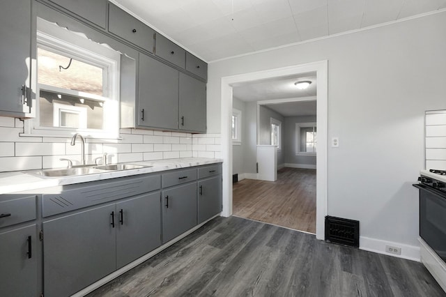 kitchen with sink, dark hardwood / wood-style flooring, backsplash, gray cabinets, and range