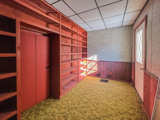 interior space featuring wooden walls, a drop ceiling, and carpet