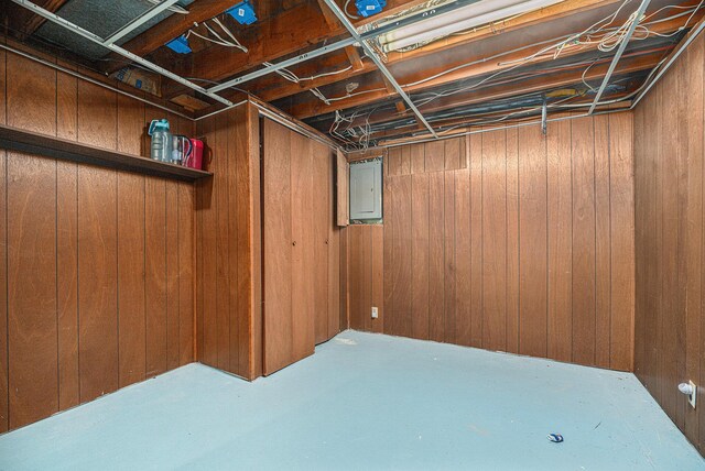 basement featuring electric panel and wooden walls