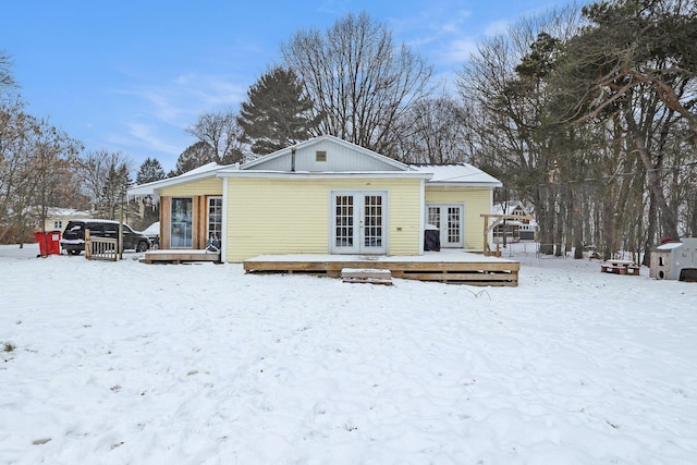 snow covered house with french doors and a deck