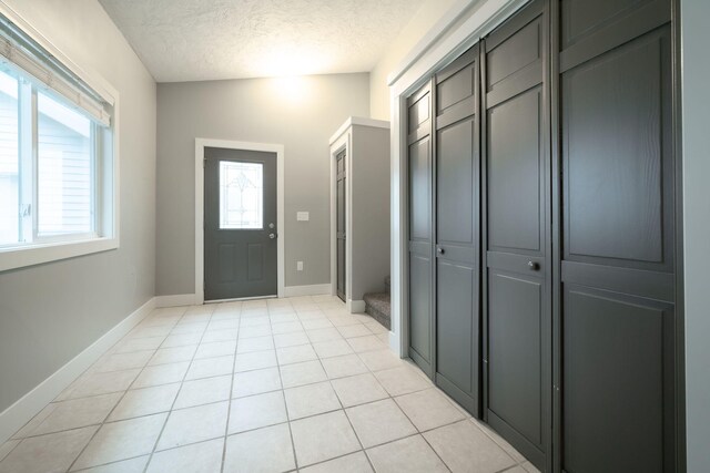 entryway with a textured ceiling, light tile patterned floors, and vaulted ceiling