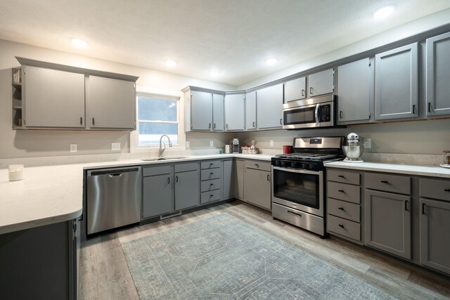 kitchen featuring appliances with stainless steel finishes, light wood-type flooring, gray cabinets, and sink