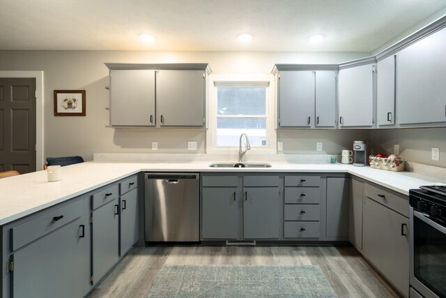 kitchen featuring stove, stainless steel dishwasher, light hardwood / wood-style floors, sink, and gray cabinets