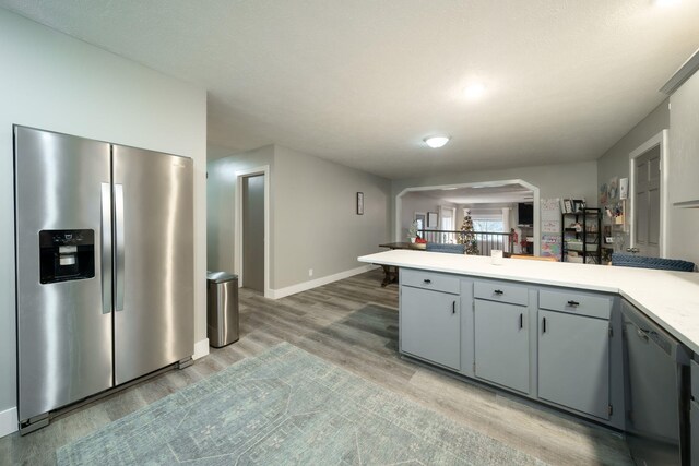 kitchen with dishwasher, stainless steel refrigerator with ice dispenser, kitchen peninsula, gray cabinets, and hardwood / wood-style flooring