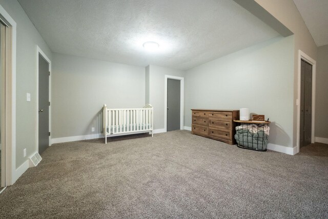 unfurnished bedroom with carpet flooring, a crib, and a textured ceiling