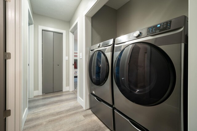 clothes washing area with light hardwood / wood-style floors, independent washer and dryer, and a textured ceiling