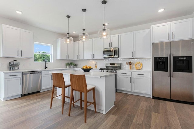 kitchen featuring stainless steel appliances, decorative light fixtures, hardwood / wood-style flooring, a center island, and white cabinetry