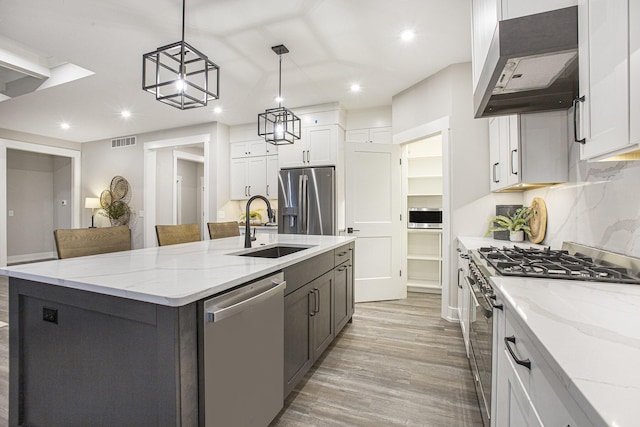 kitchen featuring stainless steel appliances, a kitchen island with sink, pendant lighting, white cabinets, and range hood