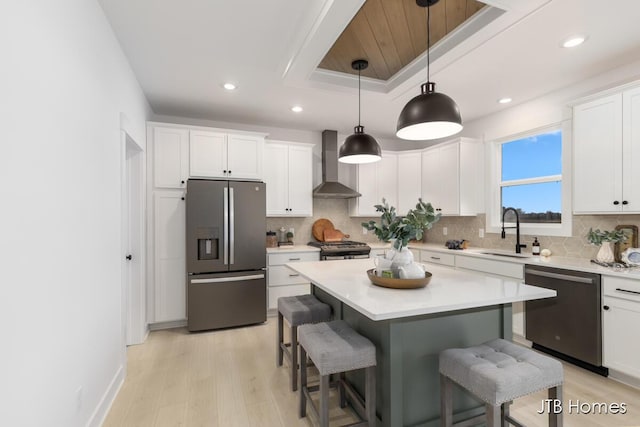 kitchen featuring a breakfast bar area, stainless steel appliances, a sink, light countertops, and wall chimney range hood