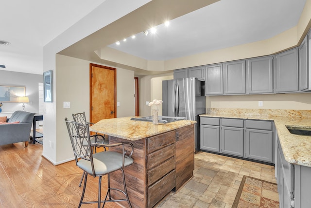 kitchen featuring a center island, light stone counters, a kitchen breakfast bar, black electric stovetop, and gray cabinetry