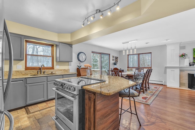 kitchen with sink, decorative light fixtures, light stone countertops, a center island with sink, and appliances with stainless steel finishes