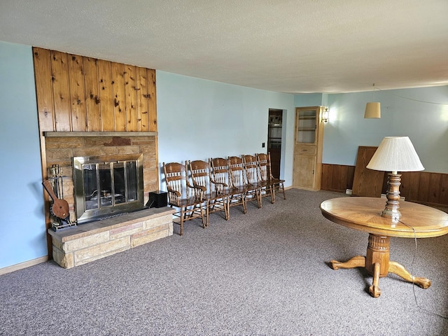 carpeted living room featuring wood walls, a fireplace, and a textured ceiling