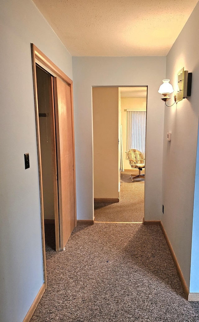 hallway featuring dark carpet and a textured ceiling