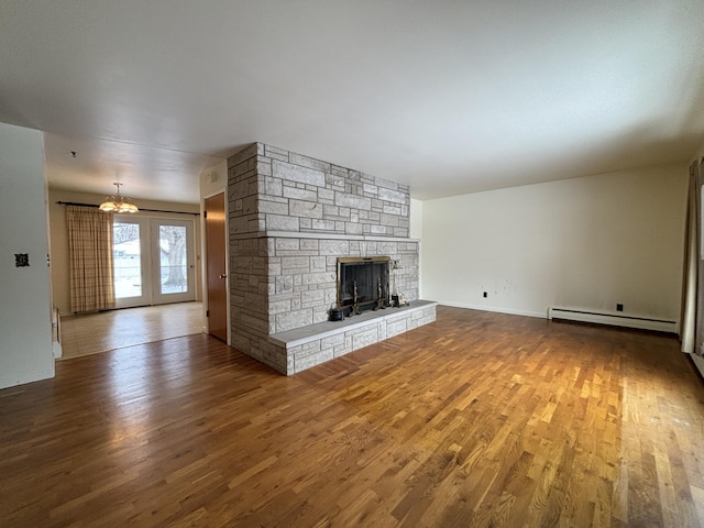 unfurnished living room featuring a baseboard heating unit, a stone fireplace, a notable chandelier, and hardwood / wood-style flooring