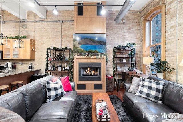 living room featuring a high ceiling, beamed ceiling, brick wall, and dark hardwood / wood-style floors