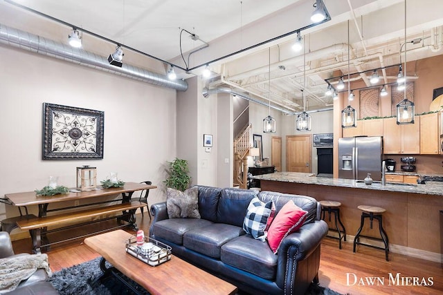 living room with a high ceiling, rail lighting, light hardwood / wood-style flooring, and sink