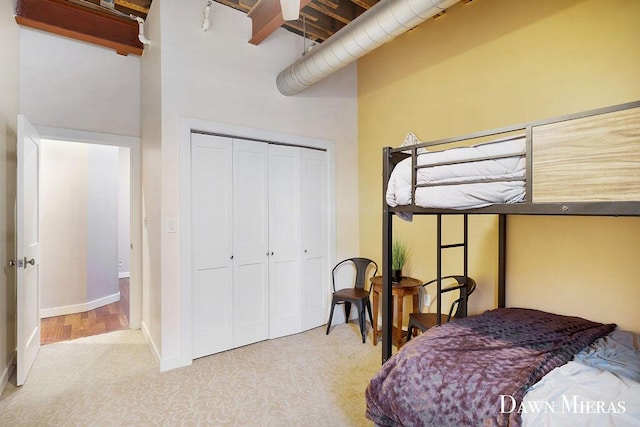 carpeted bedroom featuring beamed ceiling, a high ceiling, and a closet