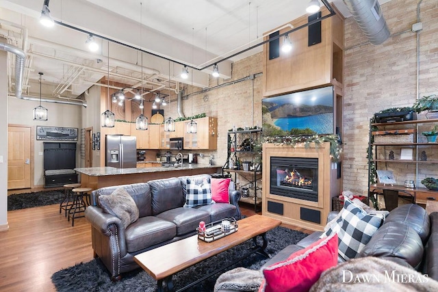 living room with sink, rail lighting, a towering ceiling, light hardwood / wood-style floors, and brick wall