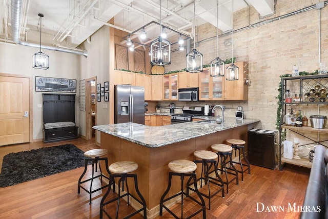 kitchen featuring kitchen peninsula, brick wall, stainless steel appliances, pendant lighting, and a high ceiling