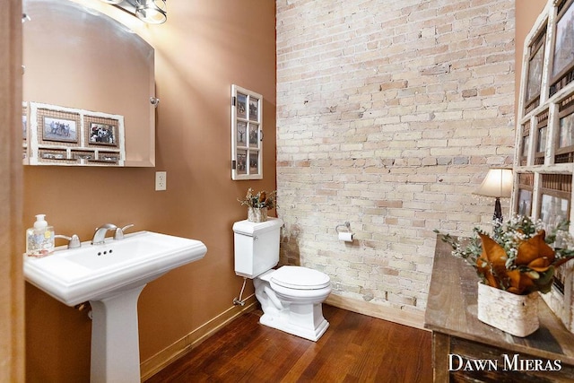 bathroom with sink, toilet, brick wall, and hardwood / wood-style flooring