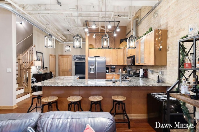 kitchen featuring hanging light fixtures, a high ceiling, brick wall, light brown cabinetry, and appliances with stainless steel finishes