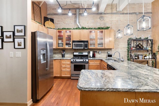 kitchen with kitchen peninsula, appliances with stainless steel finishes, sink, light hardwood / wood-style floors, and hanging light fixtures