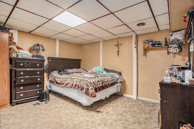 carpeted bedroom with a paneled ceiling and wood walls