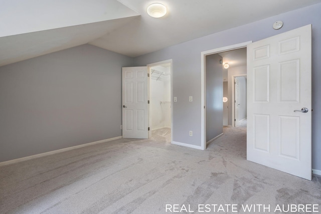 unfurnished bedroom featuring vaulted ceiling, a closet, light colored carpet, and a spacious closet