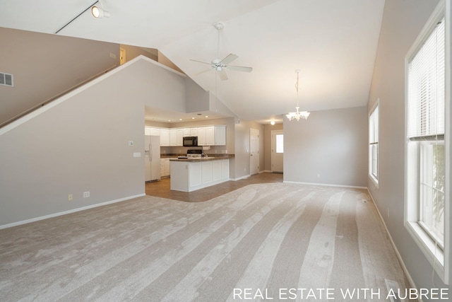 unfurnished living room with light carpet, a towering ceiling, and ceiling fan with notable chandelier