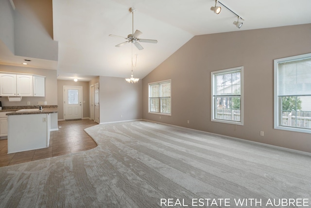 unfurnished living room with light tile patterned flooring, track lighting, lofted ceiling, and ceiling fan with notable chandelier