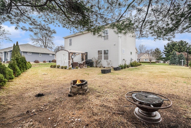 back of house featuring a fire pit, a storage unit, and a yard