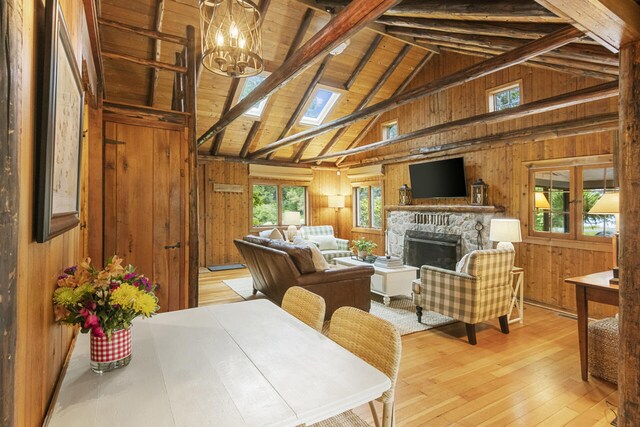 interior space featuring a stone fireplace, lofted ceiling with beams, wood walls, wood ceiling, and light wood-type flooring