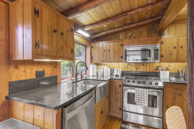 kitchen with appliances with stainless steel finishes, wooden walls, hardwood / wood-style flooring, wooden ceiling, and vaulted ceiling with beams