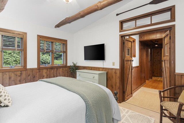 bedroom with light wood-type flooring, vaulted ceiling, ceiling fan, and wooden walls