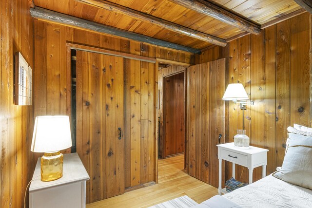 bedroom with beam ceiling, light hardwood / wood-style flooring, and wood walls