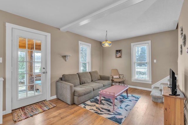 living area featuring beam ceiling, plenty of natural light, baseboards, and wood finished floors