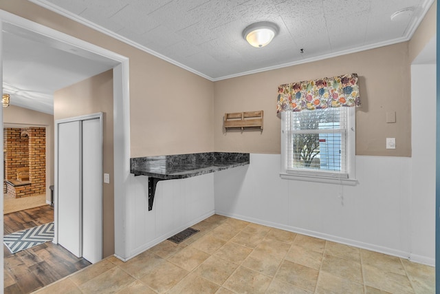 kitchen with a wainscoted wall, visible vents, and crown molding