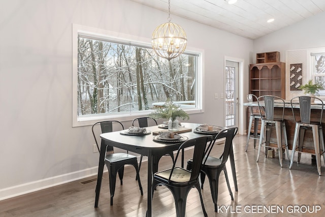 dining room with a healthy amount of sunlight, hardwood / wood-style flooring, vaulted ceiling, and a notable chandelier