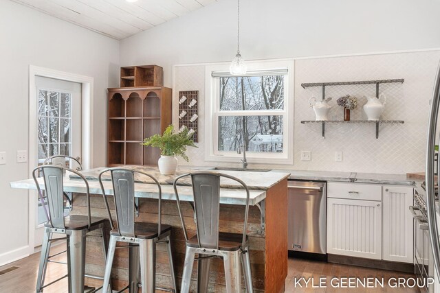 kitchen featuring lofted ceiling, stainless steel dishwasher, decorative light fixtures, light stone counters, and white cabinetry