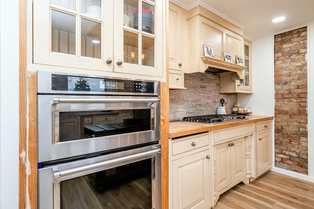 kitchen featuring stainless steel appliances, wood counters, backsplash, cream cabinets, and light wood-type flooring