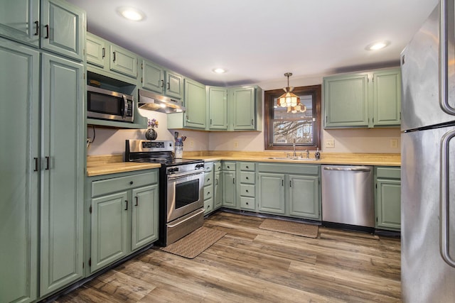 kitchen with appliances with stainless steel finishes, sink, pendant lighting, light hardwood / wood-style floors, and green cabinets