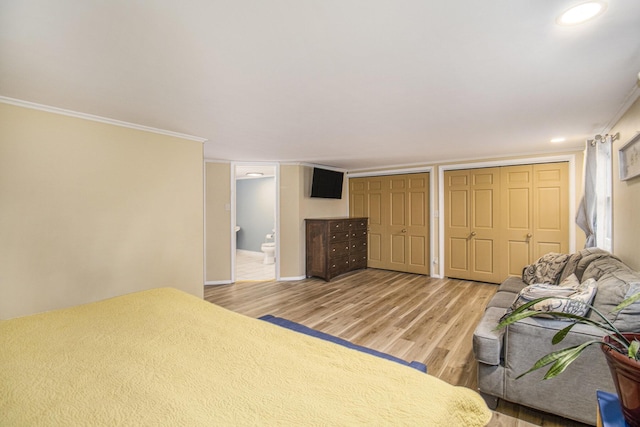 bedroom featuring ensuite bathroom, hardwood / wood-style floors, two closets, and ornamental molding