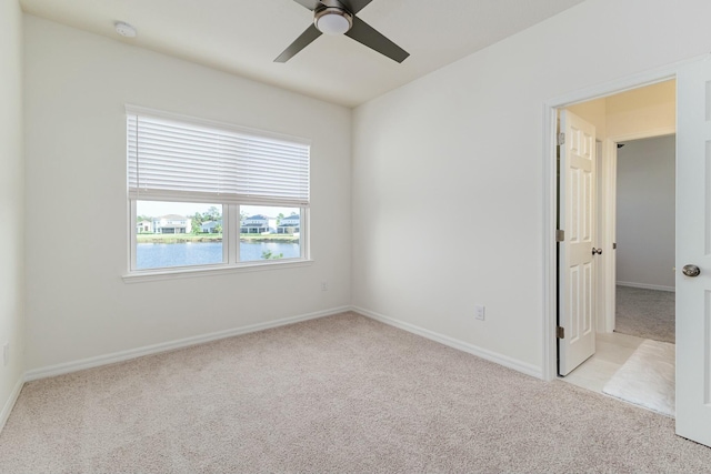 spare room with ceiling fan, a water view, and light carpet