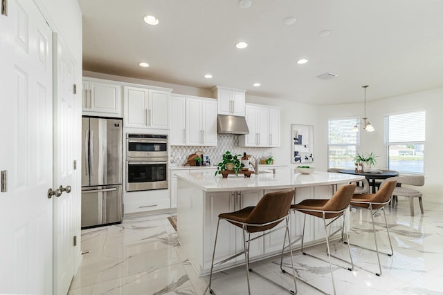 kitchen featuring tasteful backsplash, white cabinets, hanging light fixtures, and appliances with stainless steel finishes