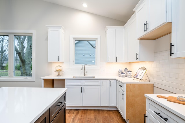 kitchen featuring white cabinetry, sink, vaulted ceiling, and light hardwood / wood-style flooring